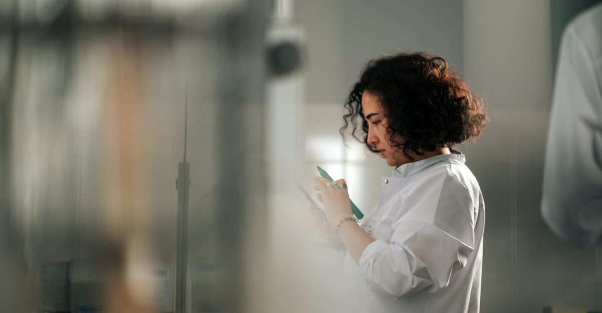 A focused female scientist with curly hair writes notes in a laboratory setting