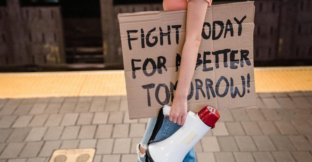 A woman stands in a subway holding a cardboard protest sign and megaphone advocating for change