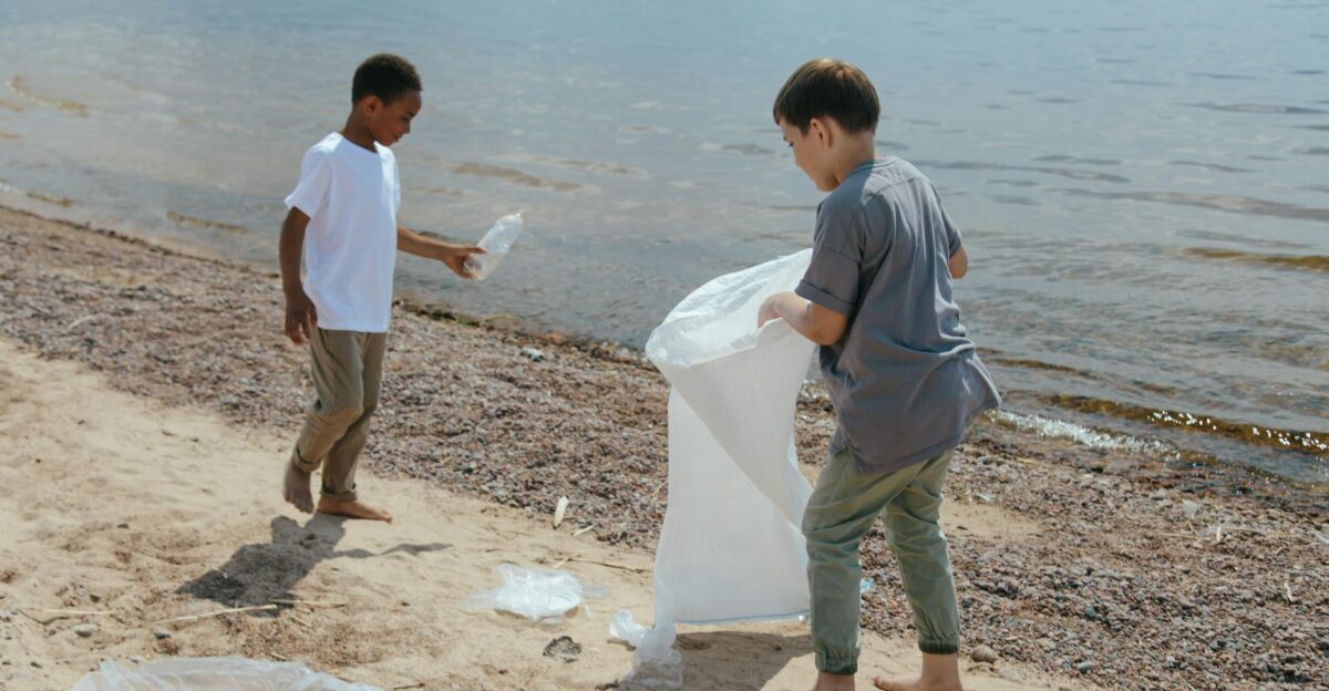 Two boys collect garbage at the beach promoting volunteerism and environmental care