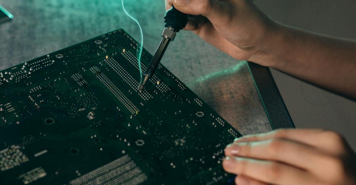 Close-up of hands soldering components on a motherboard with a soldering iron