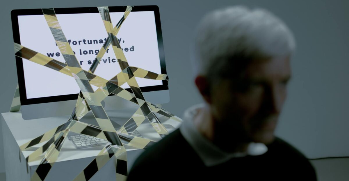 A senior man facing the reality of unemployment highlighted by a computer screen and warning tape