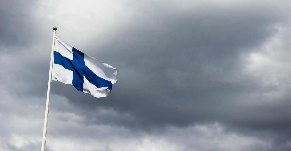 The Finnish flag waves proudly against a dramatic cloudy sky symbolizing national identity