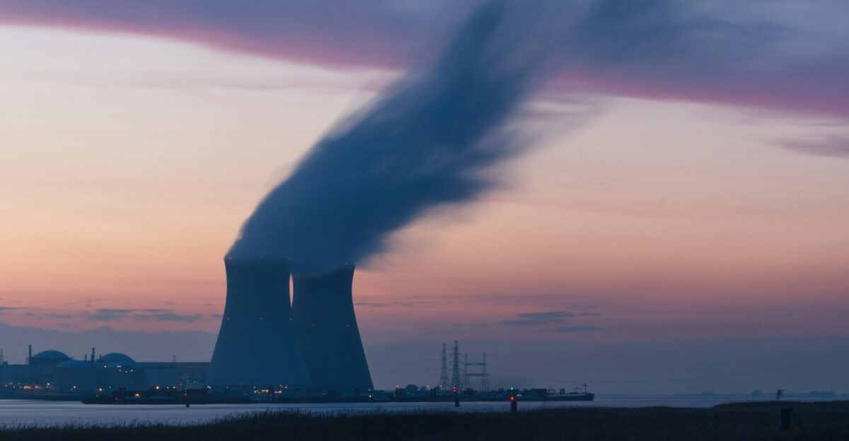 skyline photography of nuclear plant cooling tower blowing smokes under white and orange sky at daytime
