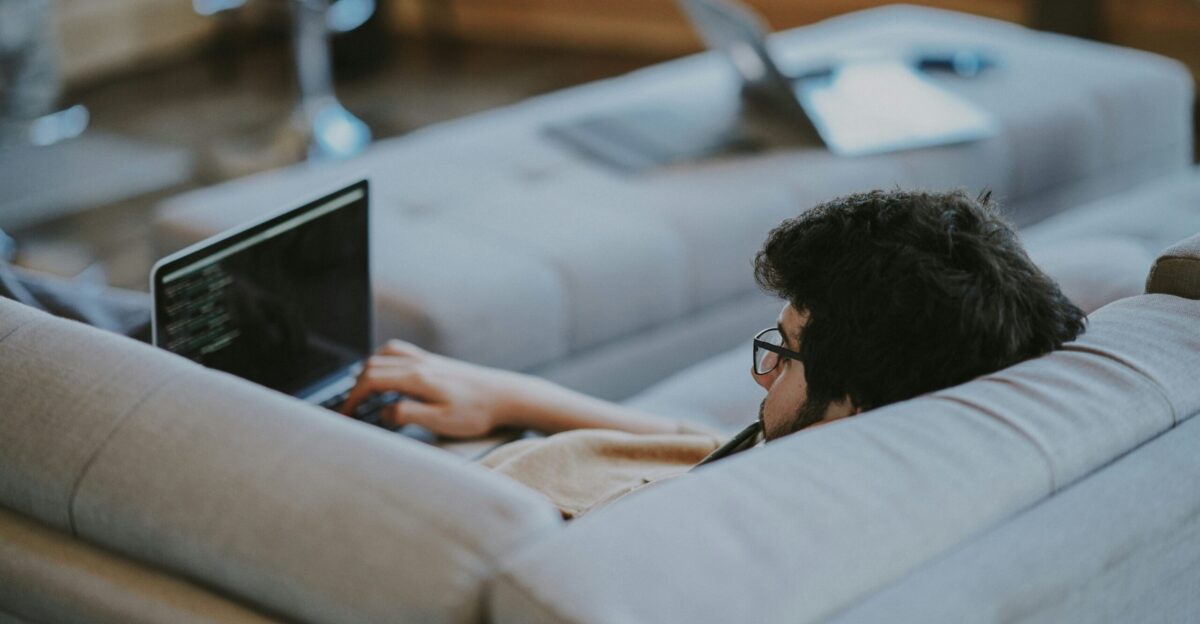 man lying on couch while using laptop computer
