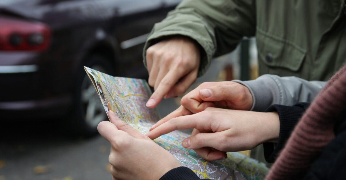 three person pointing on map near street during daytime