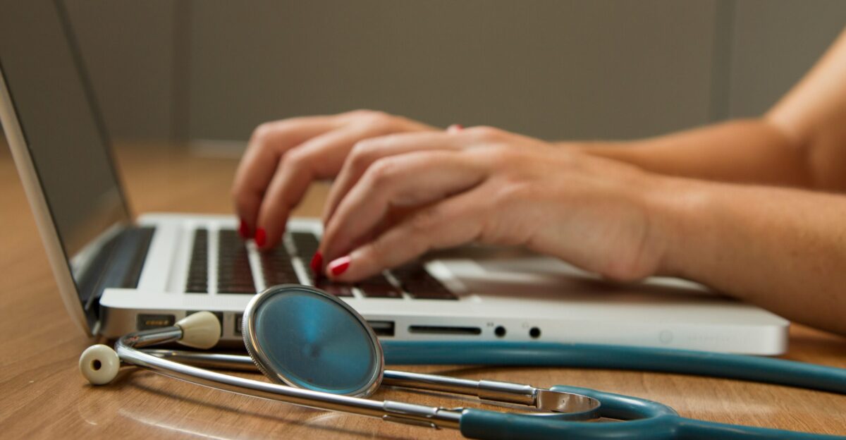 person sitting while using laptop computer and green stethoscope near