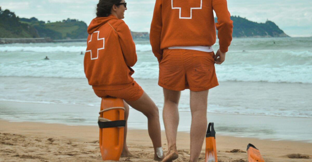 man in orange hoodie standing on beach during daytime