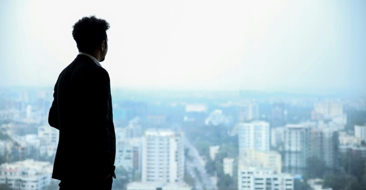 man in black suit standing on top of building looking at city buildings during daytime