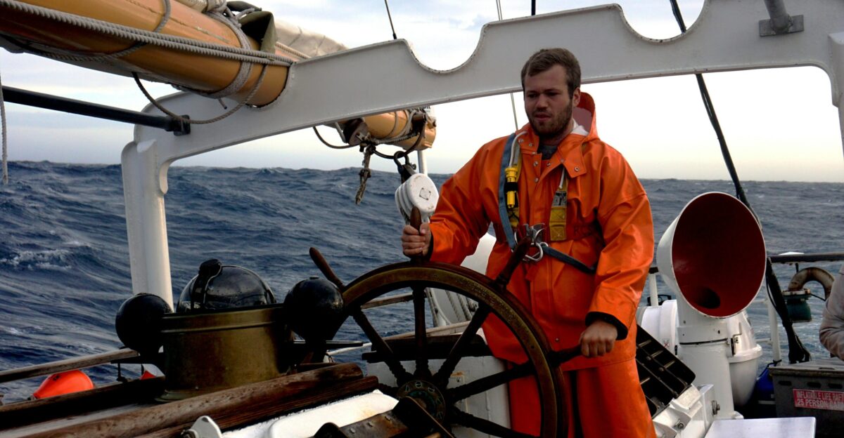man in orange jacket standing on boat during daytime