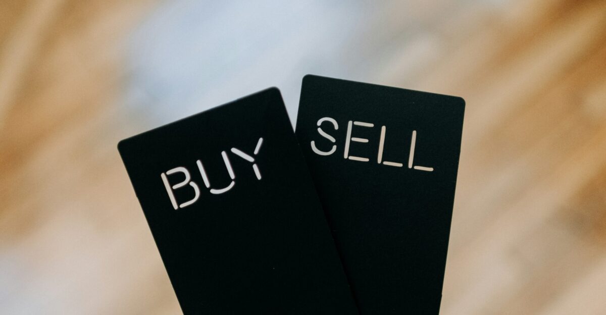 a hand holding two black cards with the words buy and sell written on them