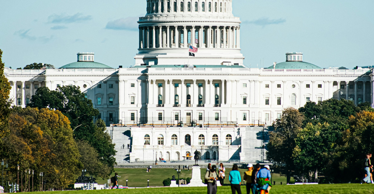 a large white building with a dome and a green lawn in front with United States Capitol in the background