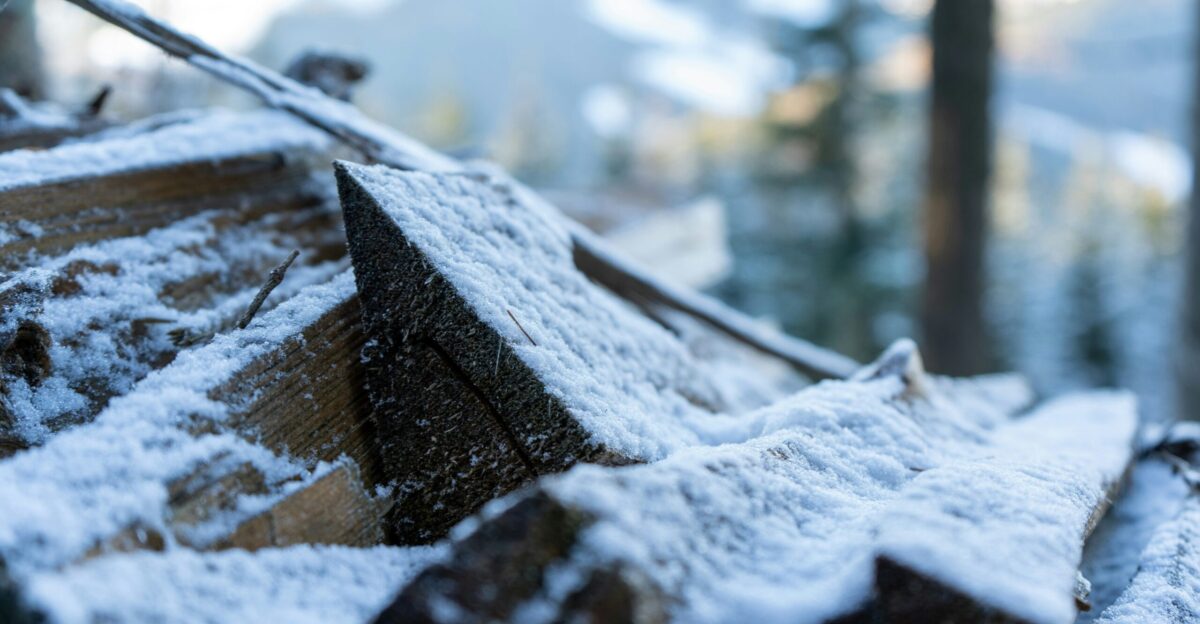 a wooden bench covered in snow next to a forest