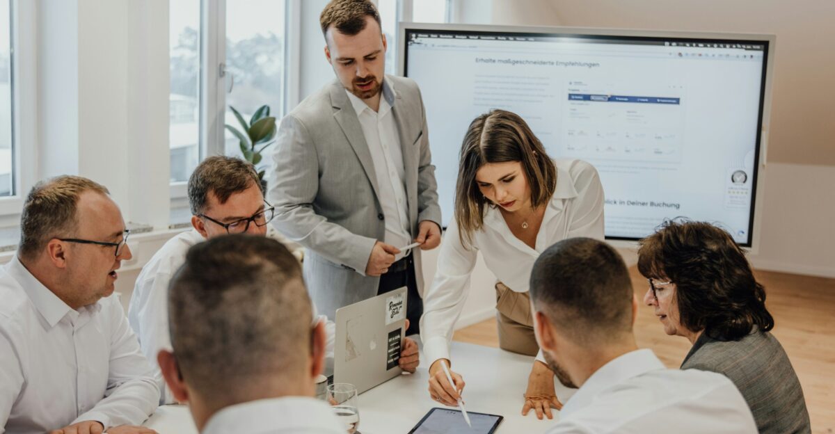 a group of people sitting around a table with laptops