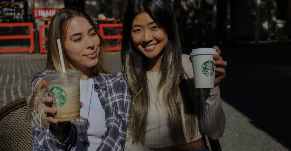 Two women sitting on a bench holding starbucks drinks