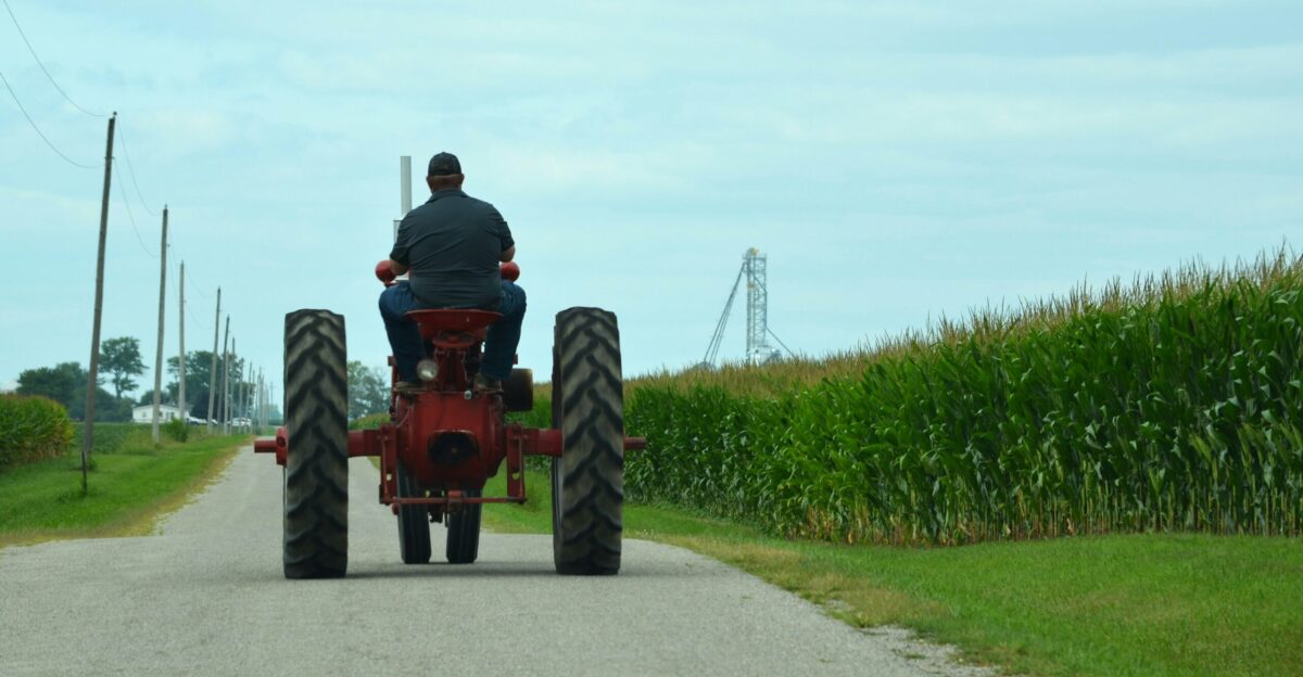A man riding on the back of a red tractor down a country road