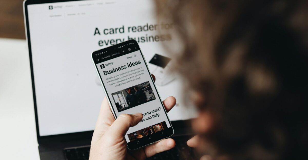 A person holding a cell phone in front of a laptop