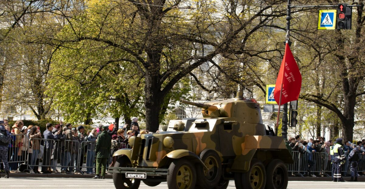 A camouflaged armored car drives through a crowd