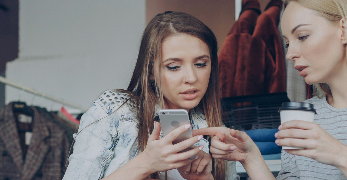 Two women are looking at a phone in a clothing store