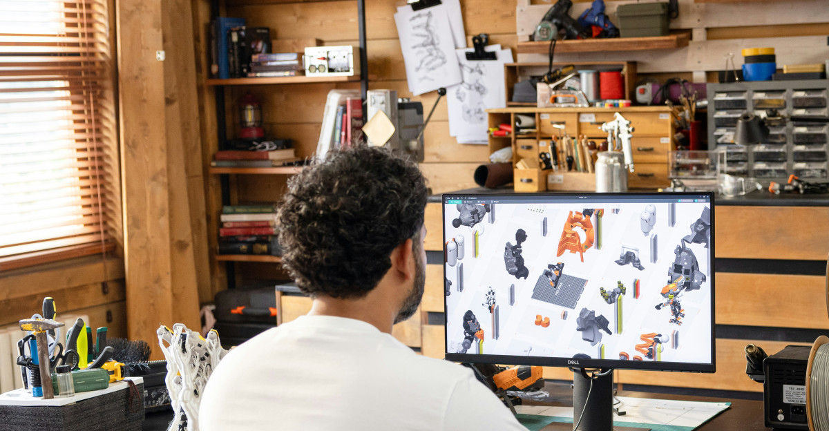 Man working on computer in a workshop with 3D printer