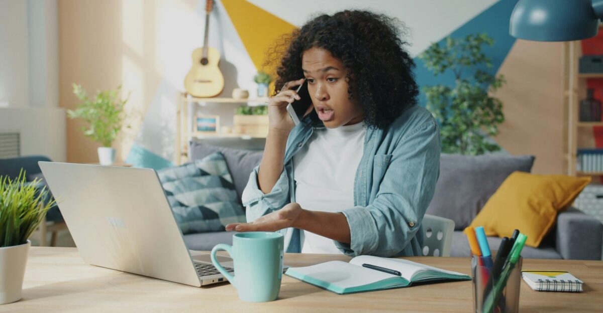 Young woman talking on phone at laptop desk