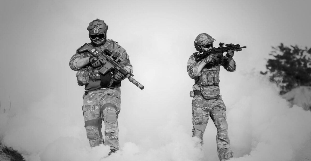 Black and white image of soldiers in a tactical operation amidst smoke and sand