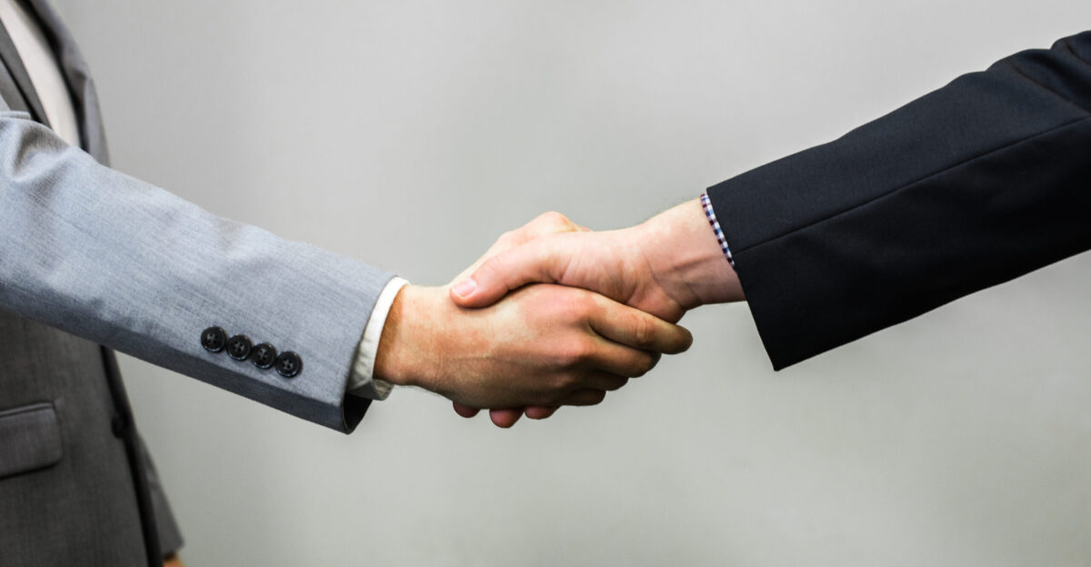 Young businessmen in suit shaking hands wide When using the image please provide photo credit link to per these terms