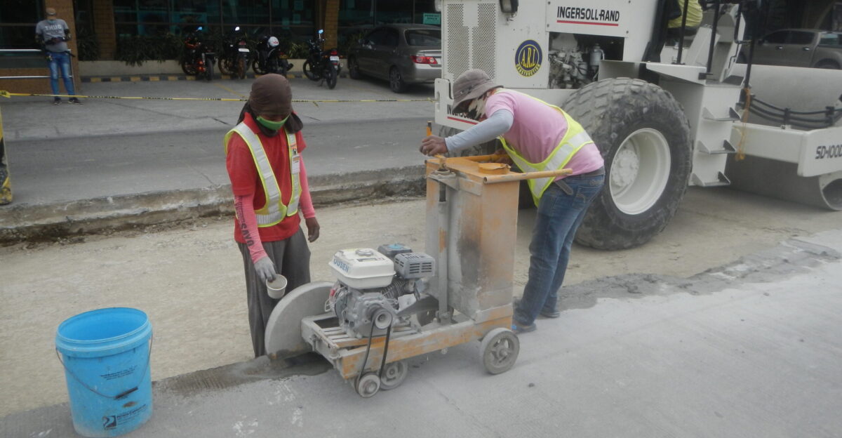 Heavy equipment operator on Ingersoll Rand SD 100D - road workers moving concrete saws to cut through MacArthur Highway Malolos City
