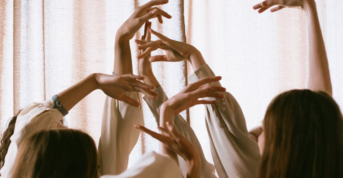 A group of women engaging in an expressive dance with arms and hands raised gracefully against a gentle backdrop