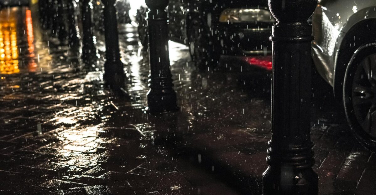 Urban street scene at night with rain and glistening pavement reflecting city lights