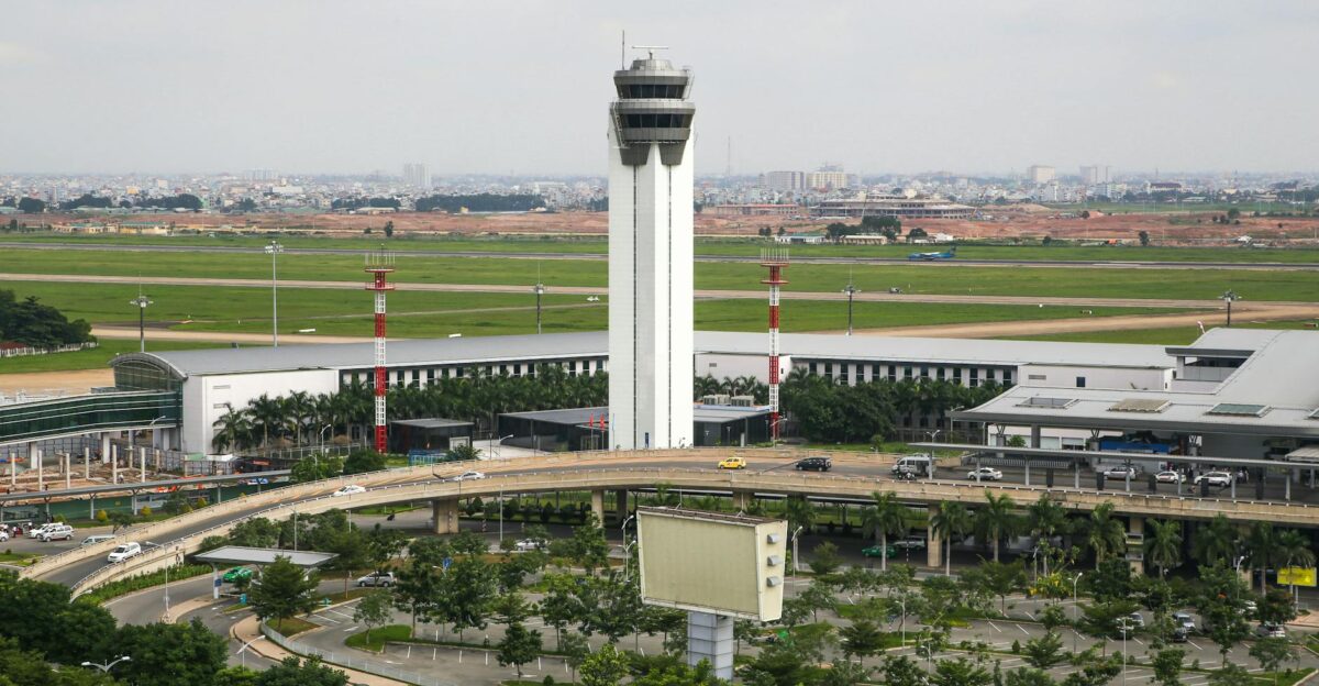 Aerial view of a busy airport with a prominent control tower surrounded by roads and greenery