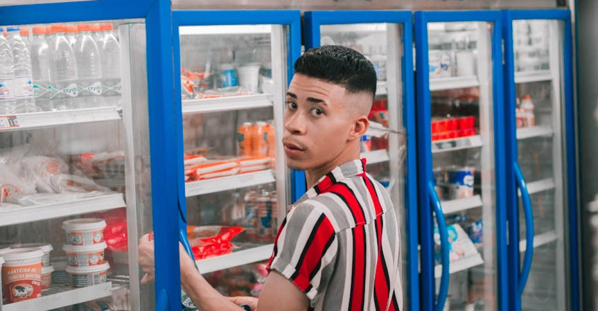 Young man in striped shirt shops from a grocery store refrigerator section