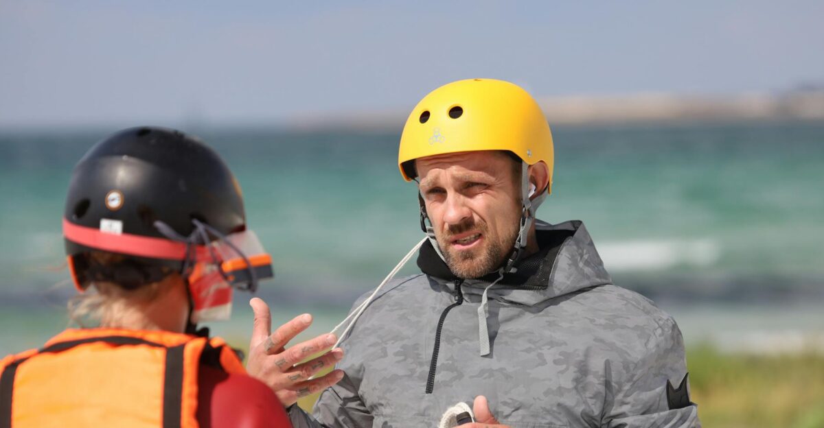 Two adults discussing safety and strategy with helmets by the sea