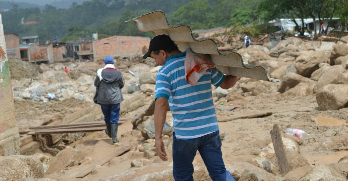 A man carries roofing material in a flood-affected area showing resilience amidst destruction