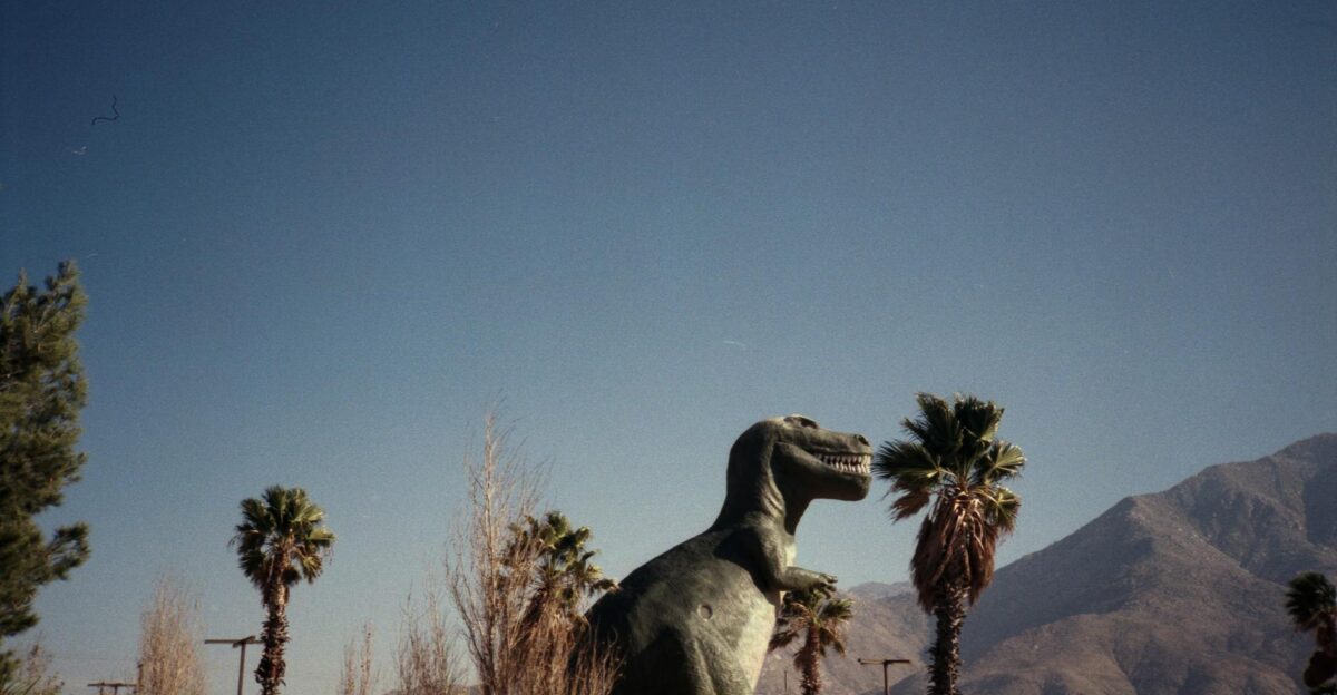 A giant dinosaur statue amidst palm trees and mountains in sunny California