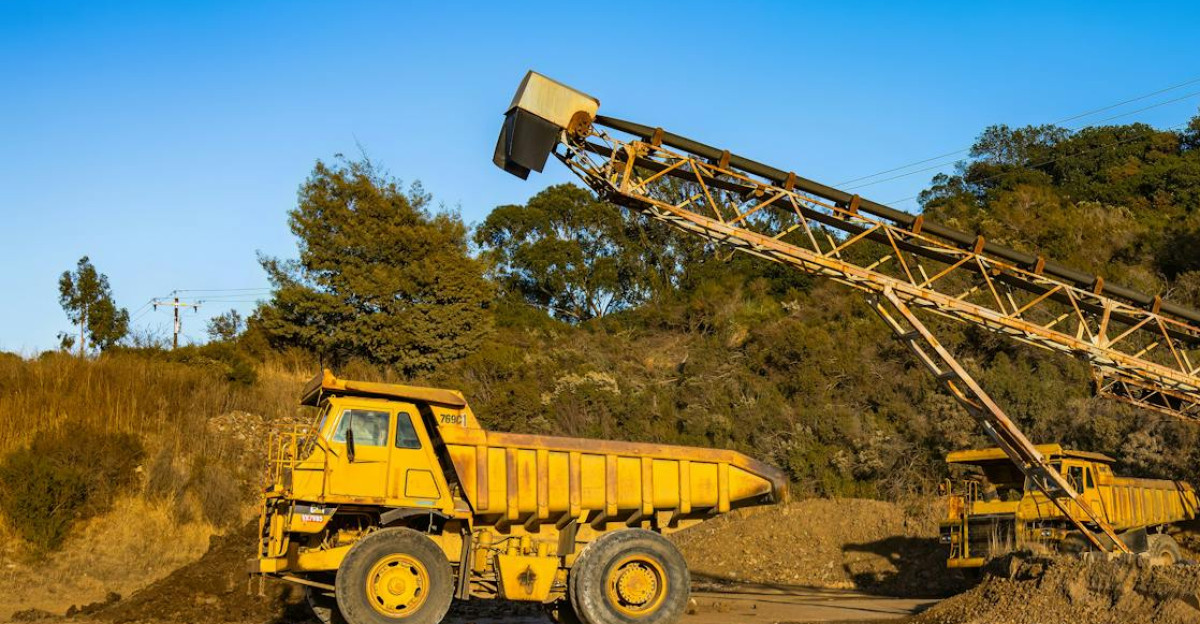 Yellow dump trucks and conveyor machinery in a sunny mining site with clear blue sky