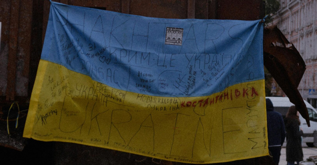 Vertical shot of a Ukrainian flag on a rusty machine in an urban setting, symbolizing conflict.