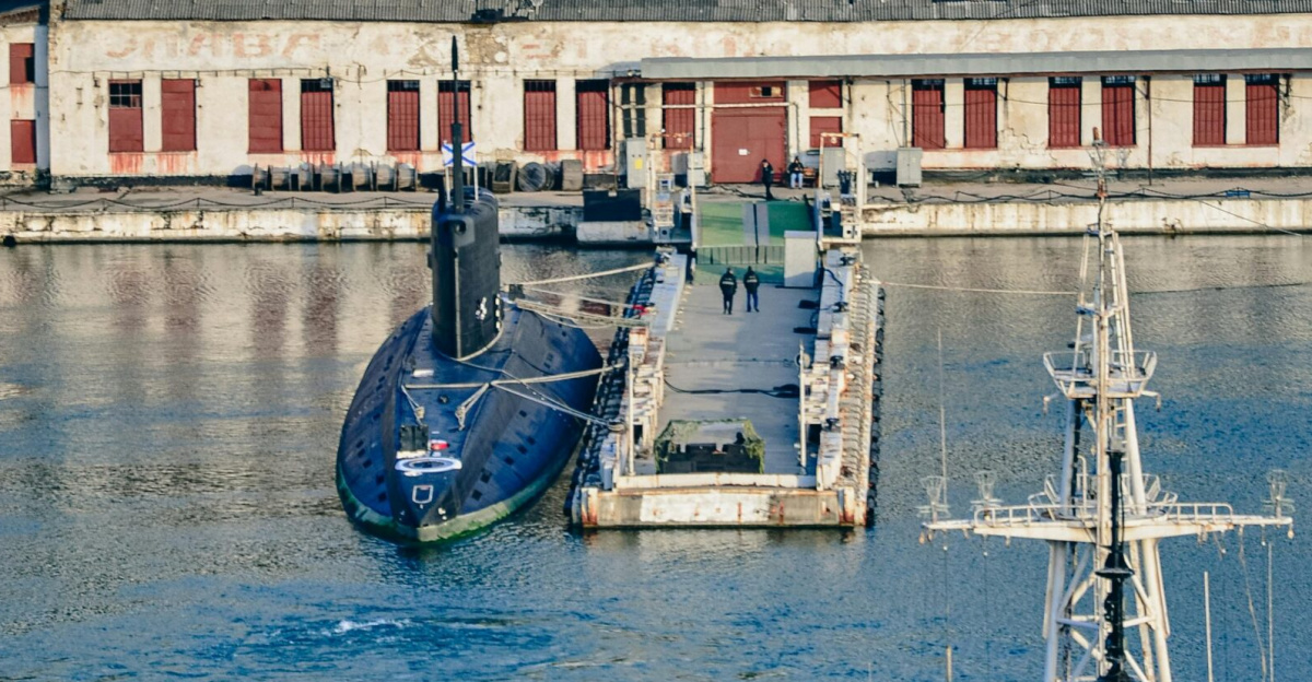 View of a submarine docked at a harbor with naval architecture backdrop.