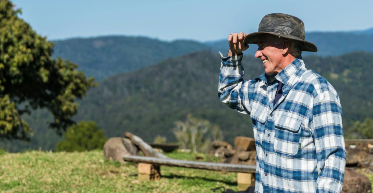A smiling farmer in plaid flannel enjoys a sunny day on a lush green hillside