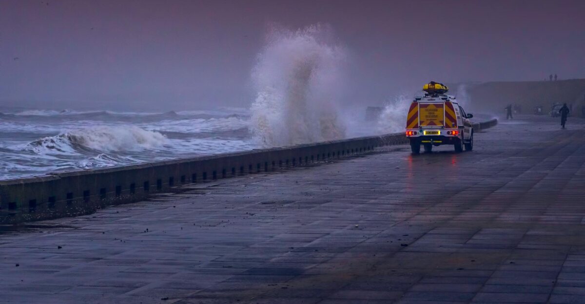 A dramatic coastal scene with waves crashing against a seawall and a vehicle on a stormy day