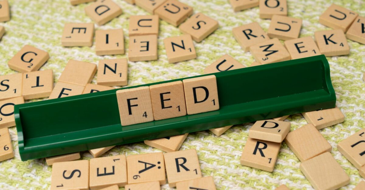 Scrabble tiles spelling FED on a green rack surrounded by scattered tiles on a textured surface