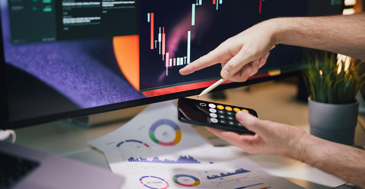 Hands analyzing stock market data on monitor and smartphone in office setting