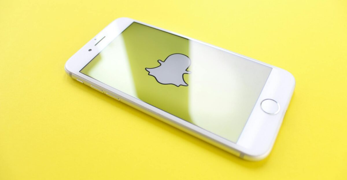 White smartphone displaying Snapchat logo on a bright yellow background angled view