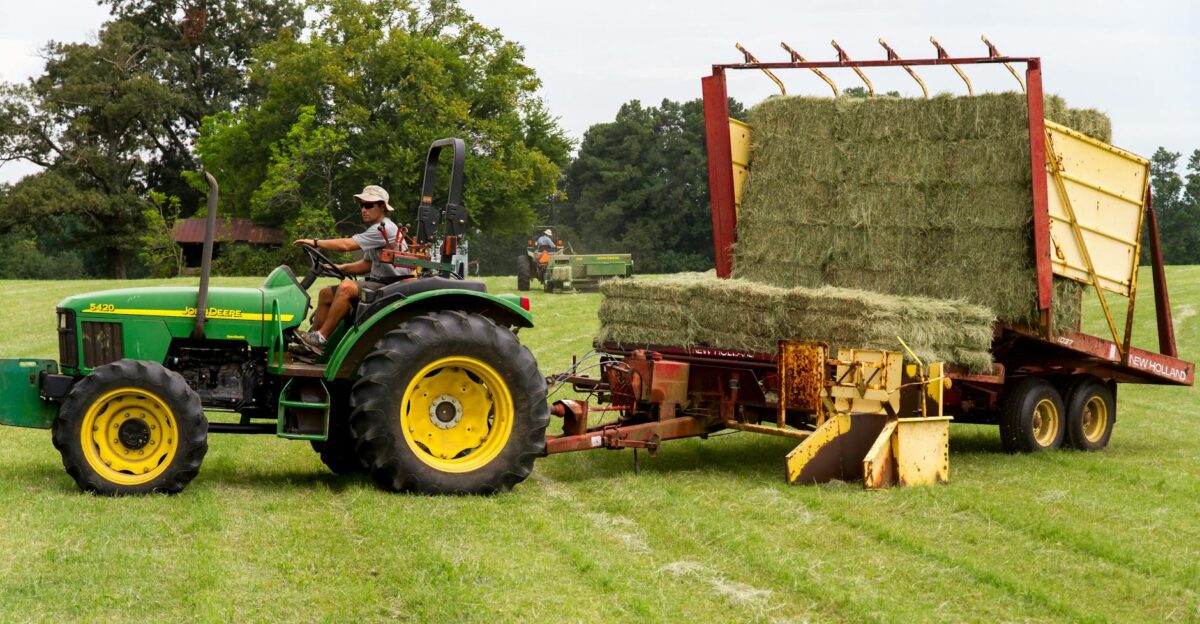 A farmer operating a green tractor loading hay in a rural North Carolina field