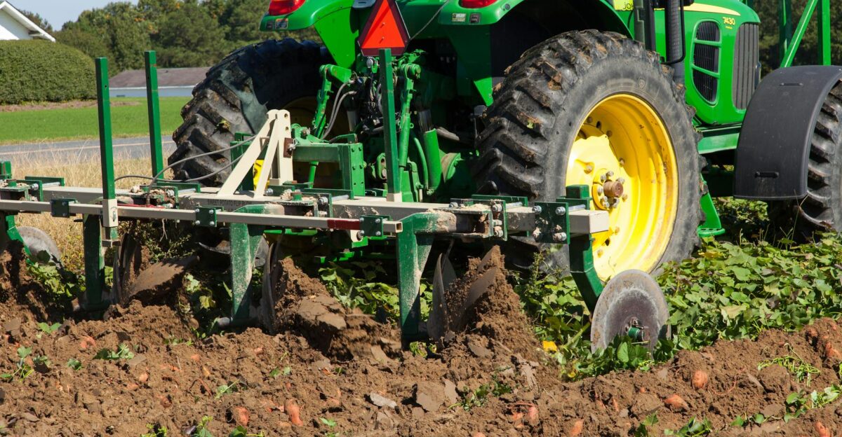 A green tractor plowing a field in North Carolina during summer Agriculture machinery and crops visible