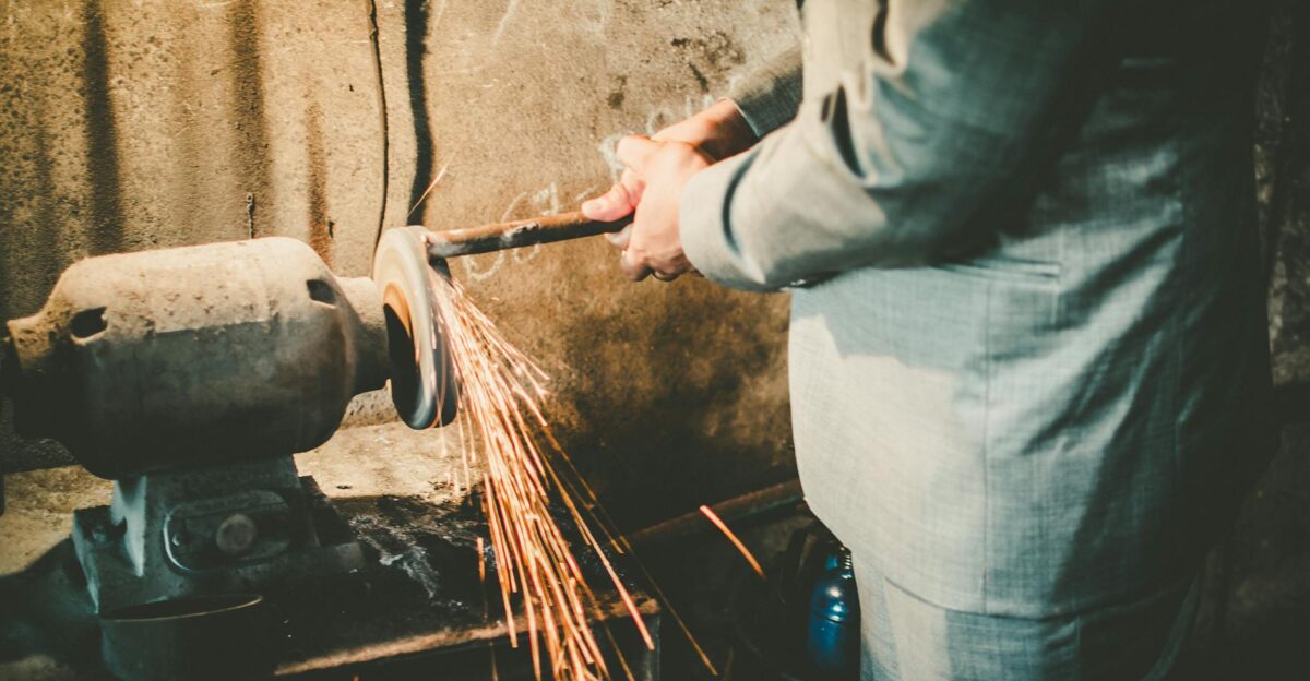 Close-up of a man in a suit using a grinder in an industrial setting with sparks flying