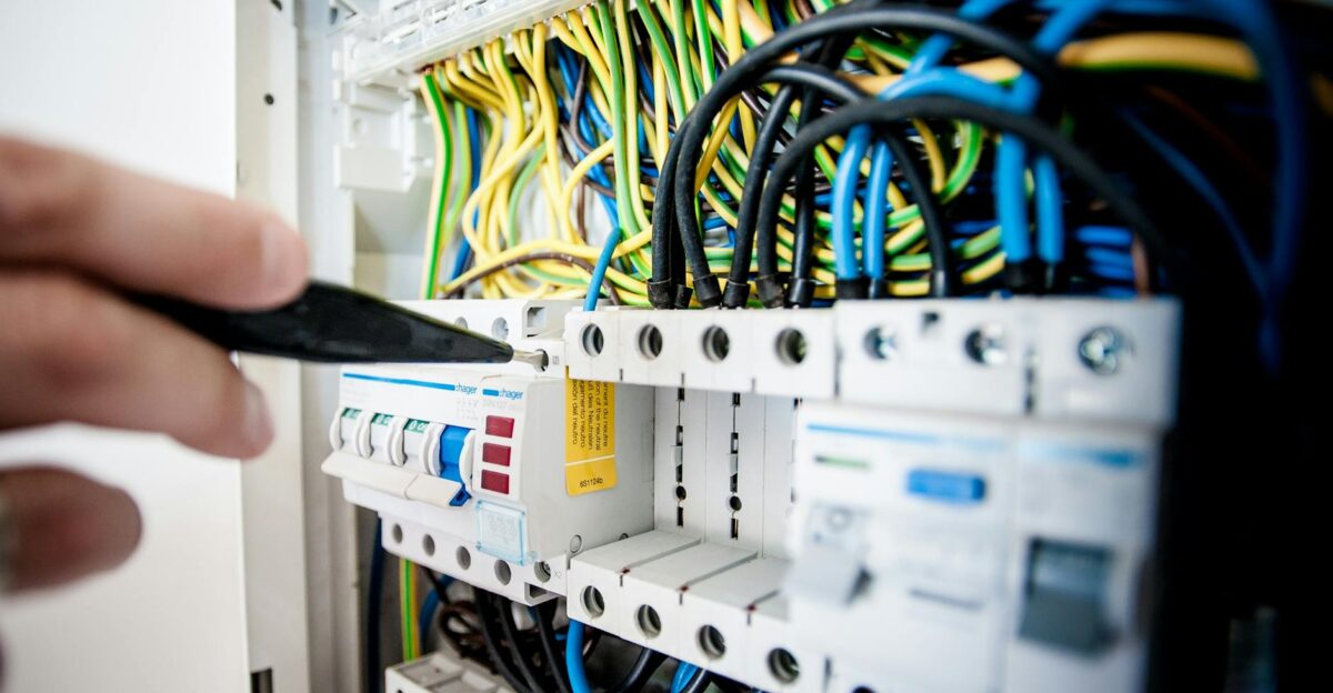 Hand of electrician working on a circuit breaker panel with colorful wires ensuring safe electrical connections