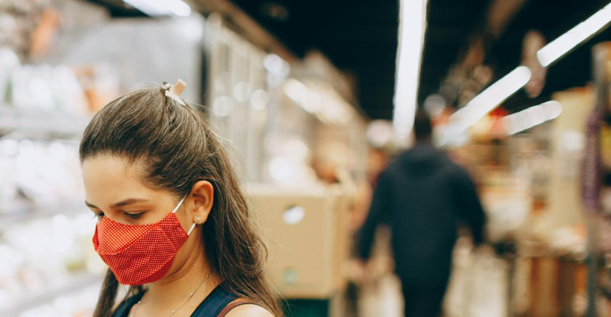 A woman wearing a mask shops for groceries in a supermarket checking products with her phone