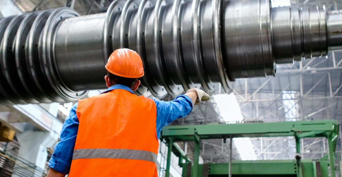 Engineer in high visibility vest and hard hat inspecting large machinery in factory setting