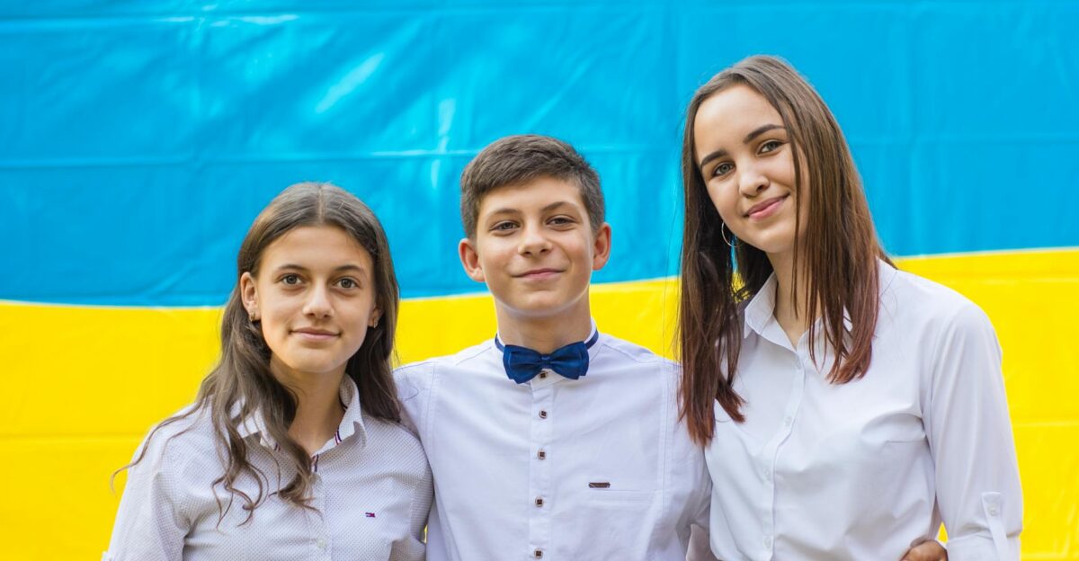 Three Ukrainian teenagers smiling in front of their national flag embracing friendship