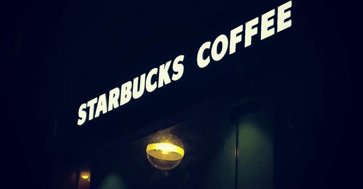 A glowing Starbucks coffee shop sign illuminates the night with a cozy ambiance